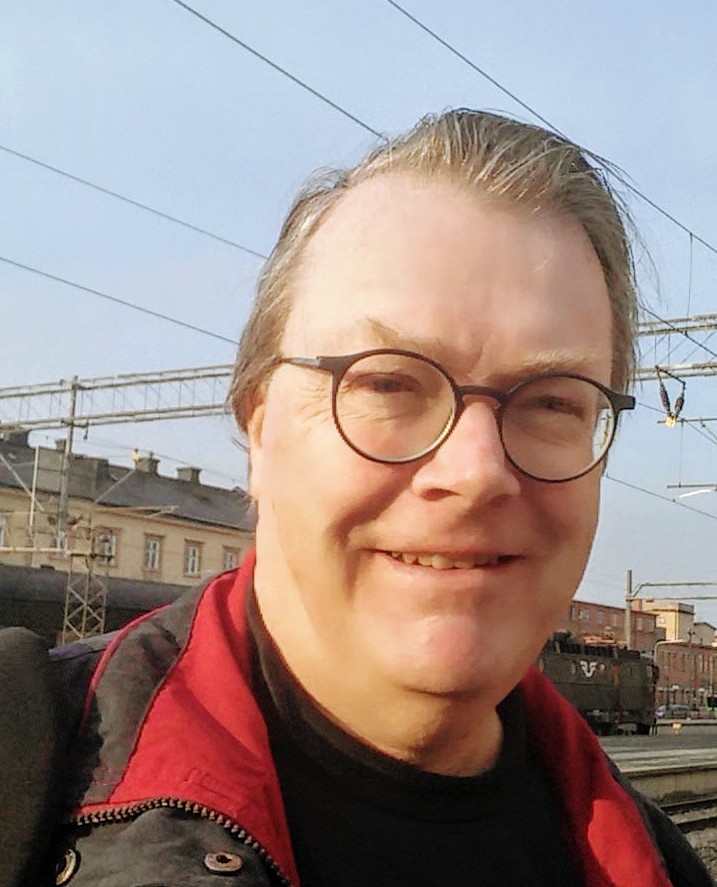 Portrait of  Johan Rudborg with buildings and a train in the background.