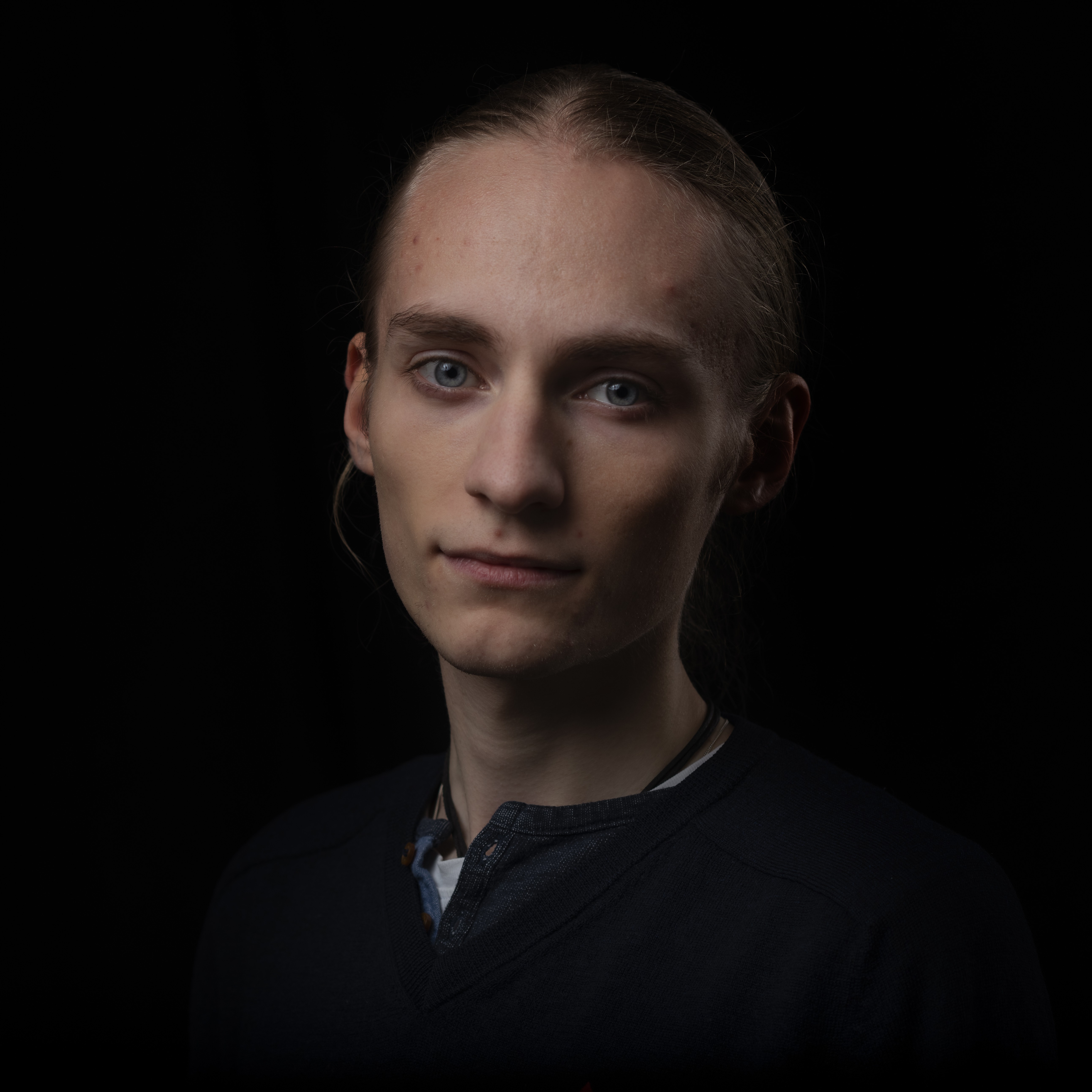 Porträtt av Simon. Bakgrunden är mörk, och endast hans ansikte är synligt.
